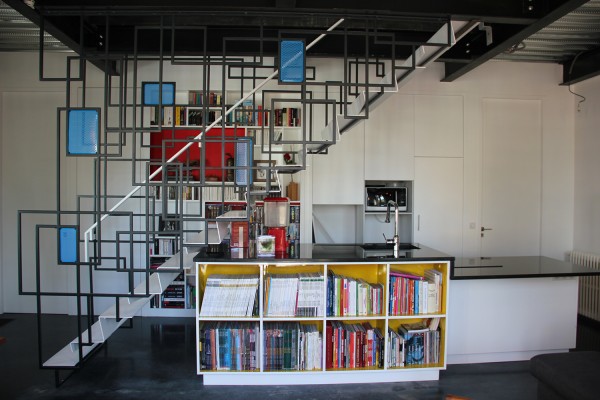Maison des charmilles - Mondrian - Escalier suspendu à la trémie de l'étage, cuisine/bibliothèque intégrée dessous, et mur de rangements en fond, portes toute hauteur. / © Justine Reverchon Architecte