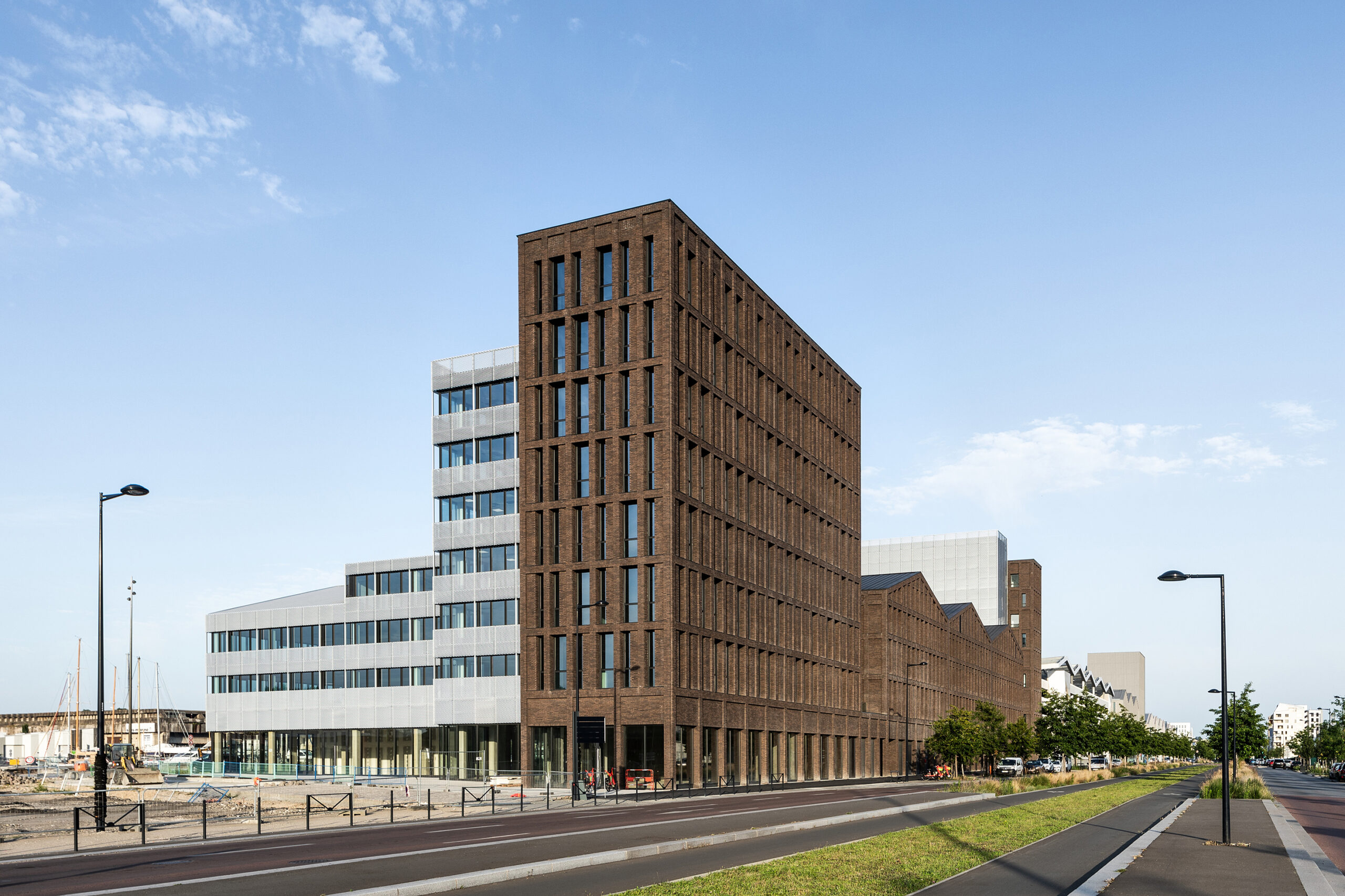 la hauteur des bâtiments diminue progressivement côté bassins et les façades s’habillent d’une résille de métal déployé en aluminium anodisé / Ivan Mathie